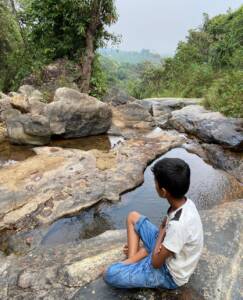 Young guest sitting on rocks by a natural stream near Astagiri Homestay, Chikmagalur
