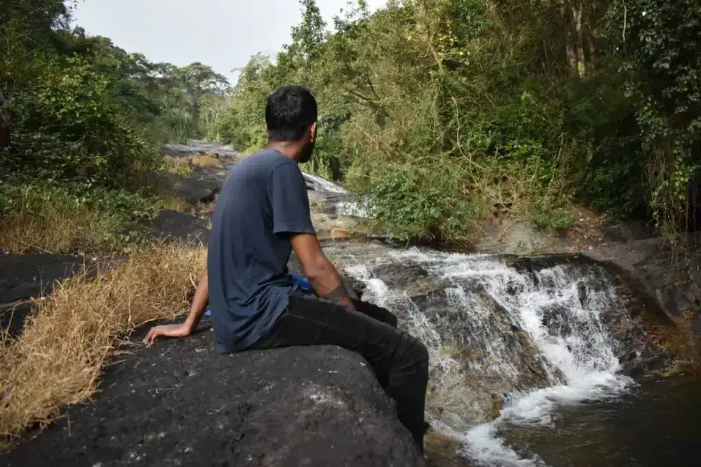 Guest sitting on rocks beside the Astagiri waterfall in mudigere, Chikmagalur.